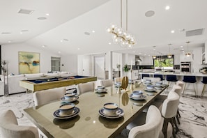 Uma cozinha moderna com ilha central, armários brancos e um espaço de refeições com uma mesa comprida para seis pessoas.