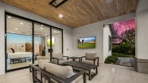 A modern living room with a large glass door leading to a bedroom, a flat-screen TV mounted on the wall, and a view of a golf course through the glass.