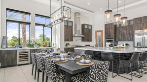 A modern kitchen with a large island, dark wood cabinets, and pendant lighting. - Palm Villa- Luxury 7 Bed, Pickleball, Volleyball, Golf (Indio)