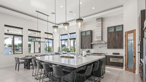 A spacious kitchen with a large island, modern pendant lights, and a view of the outdoors. - Palm Villa- Luxury 7 Bed, Pickleball, Volleyball, Golf (Indio)
