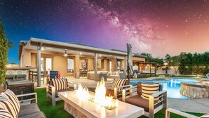 A modern outdoor living area with a fire feature, pool, and comfortable seating. - Pura Vida: Waterslide, Mini Golf, and Games! (Indio)