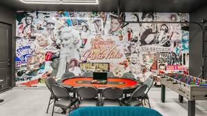 A room with a round table, chairs, a foosball table, and a wall decorated with various posters and images. - Pura Vida: Waterslide, Mini Golf, and Games! (Indio)