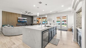 A modern kitchen with a large island, built-in appliances, and a dining area with a curved sofa. - Pura Vida: Waterslide, Mini Golf, and Games! (Indio)