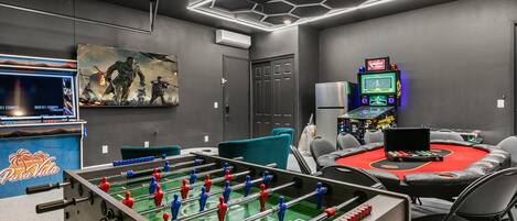 Une pièce équipée d’un baby-foot, d’une table de billard et d’un espace de jeux avec des bornes d’arcade.
