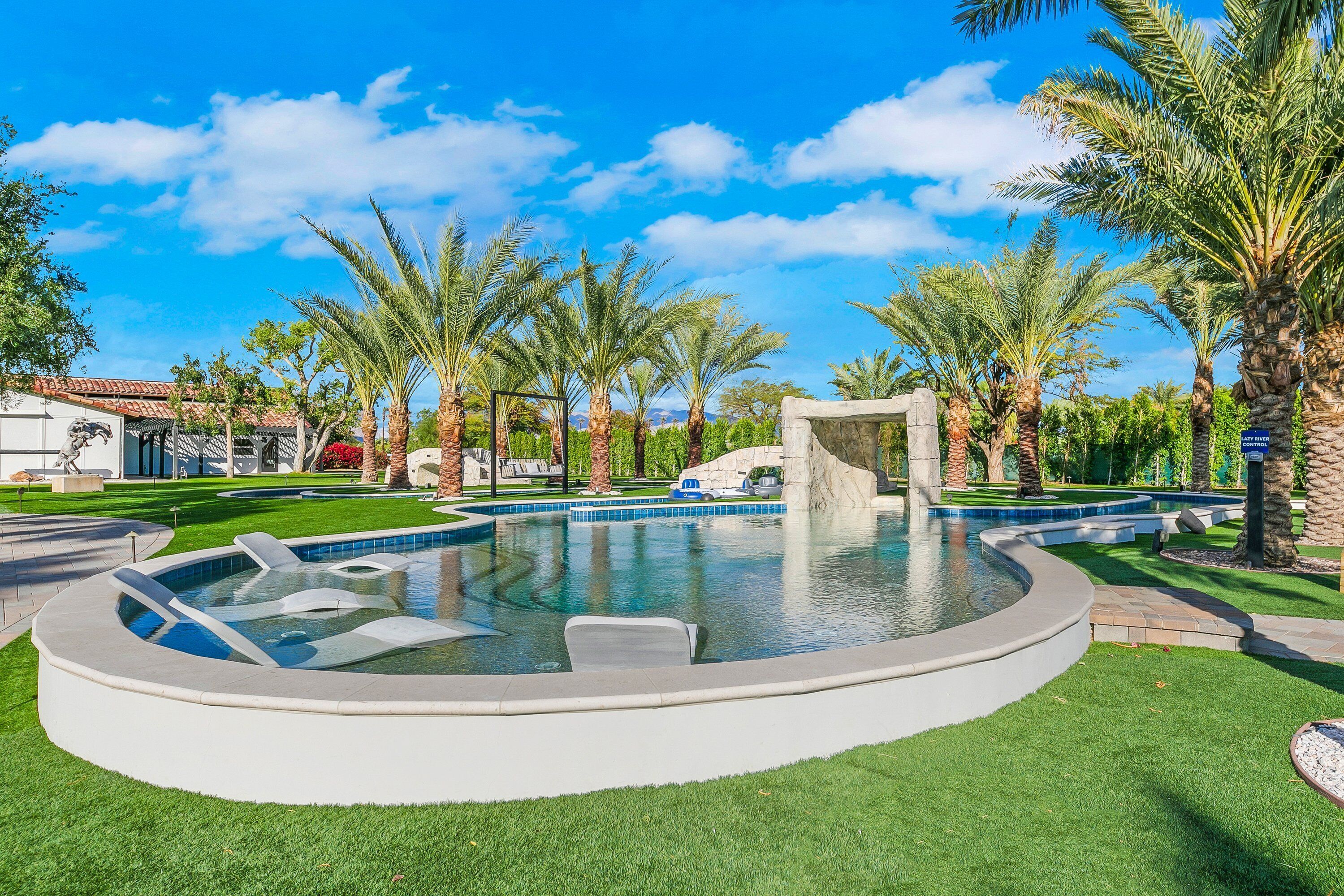A circular pool with a stone structure in the center, surrounded by palm trees and well-maintained grass.