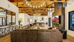 A spacious living area with a large sectional sofa, a dining table, and a kitchen in the background. - The Stallion Estate Sleeps 24, Theater, Game Room, Pickle Ball (Indio)