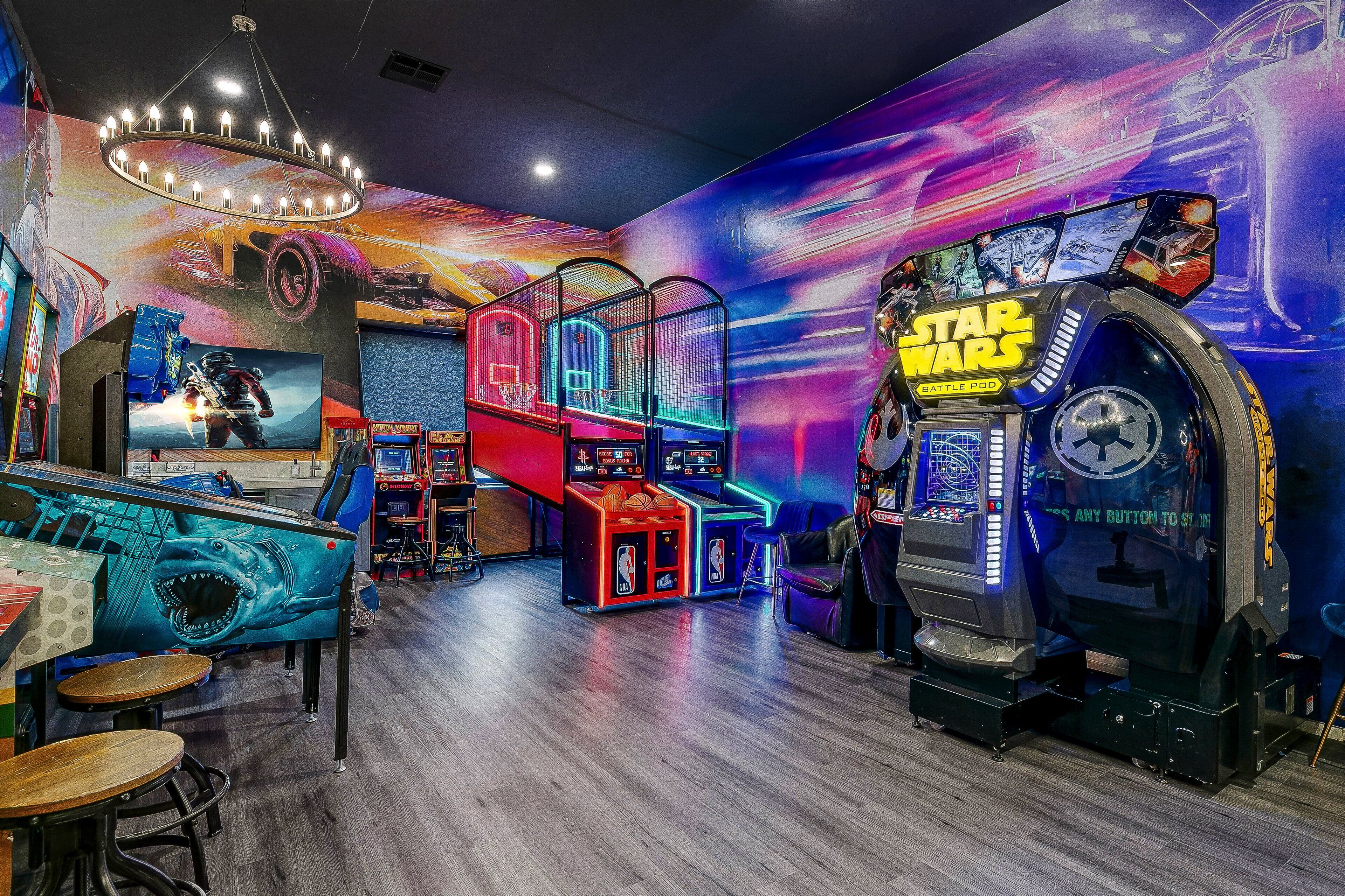 A brightly lit arcade with various gaming machines, including a Star Wars battle pod, and a large mural on the wall.