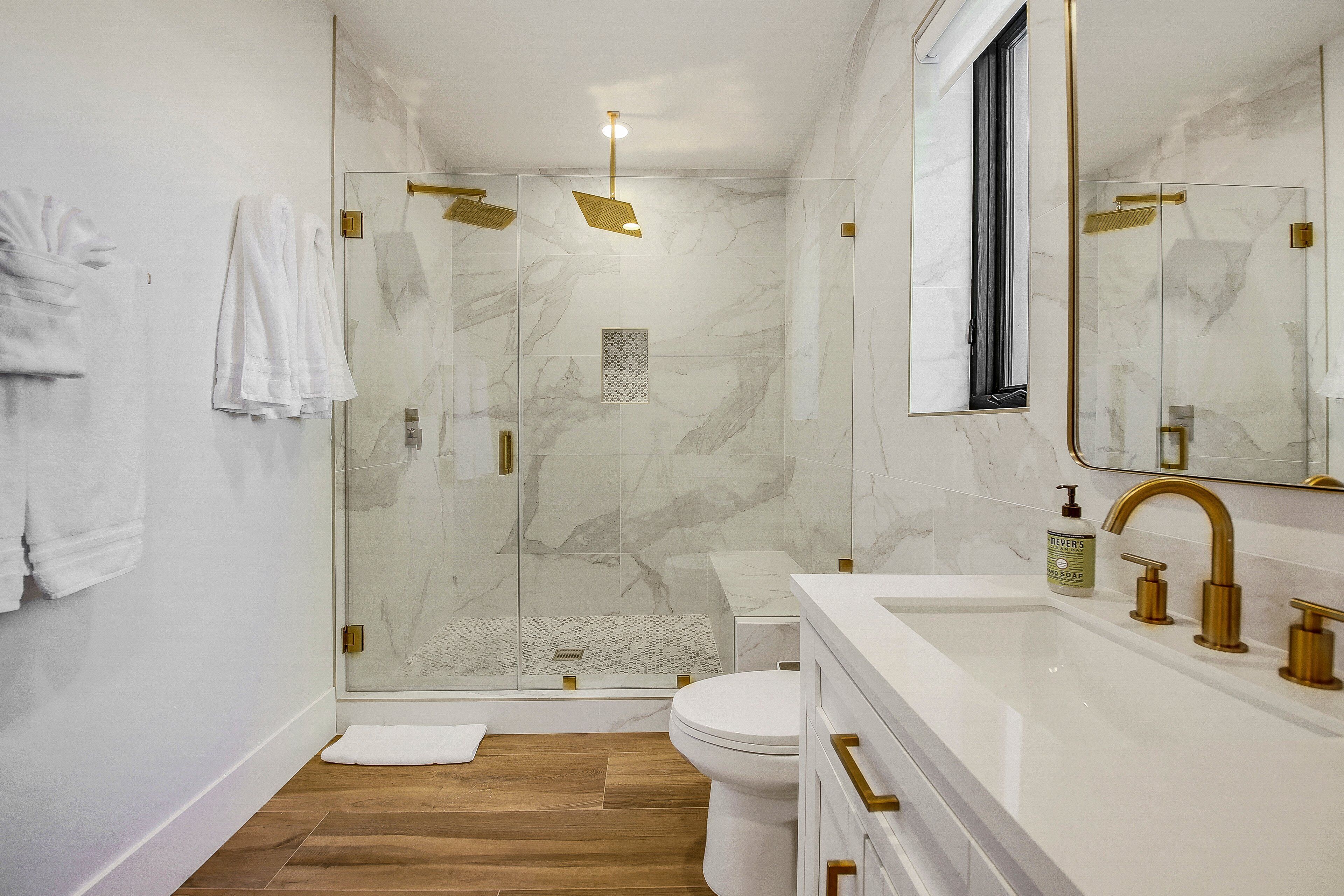 A modern bathroom with a glass-enclosed shower, a white sink with gold fixtures, and a marble-tiled wall.