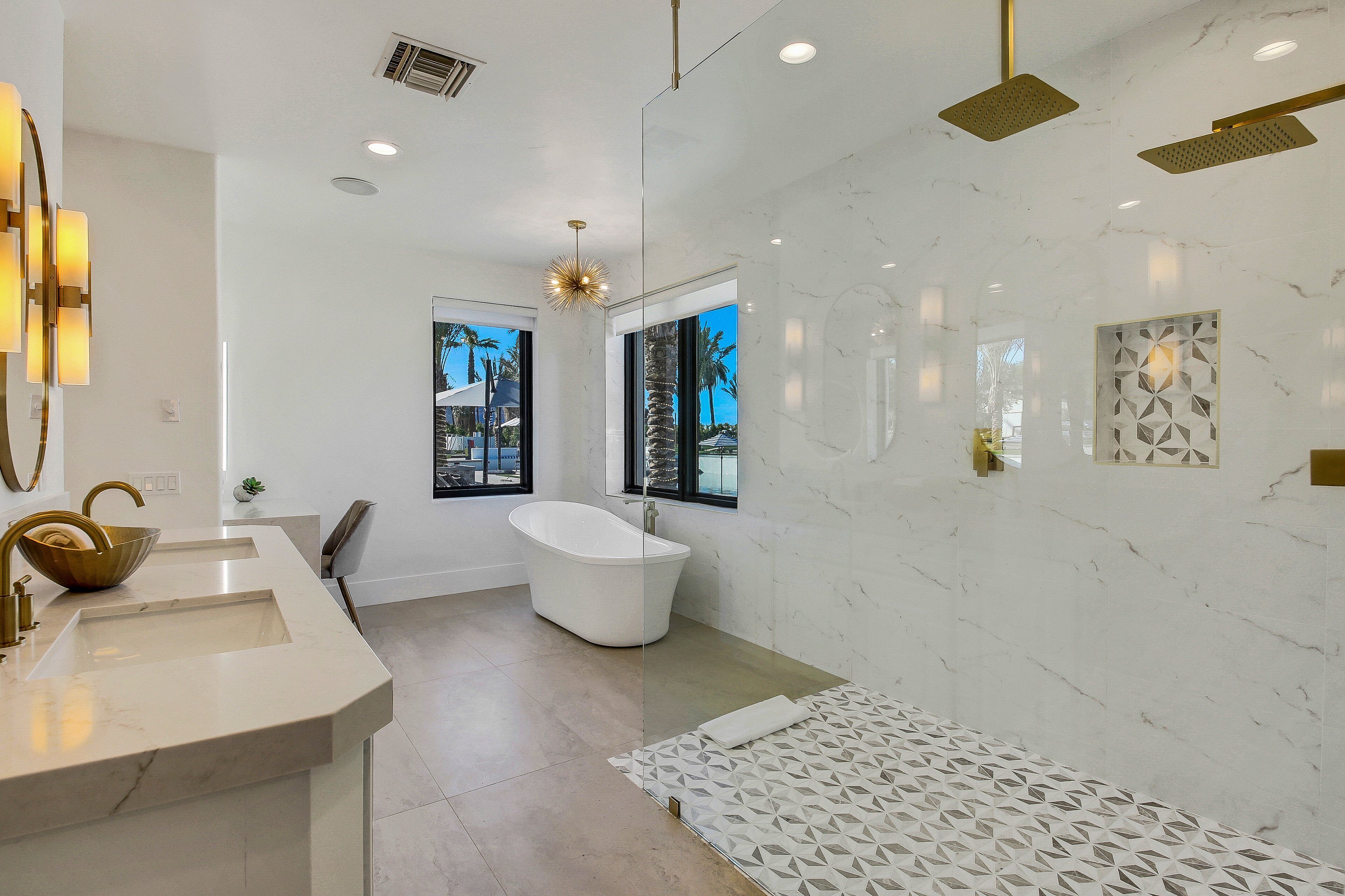 A modern bathroom with a freestanding bathtub, a large vanity with a gold faucet, and a geometric-patterned rug.
