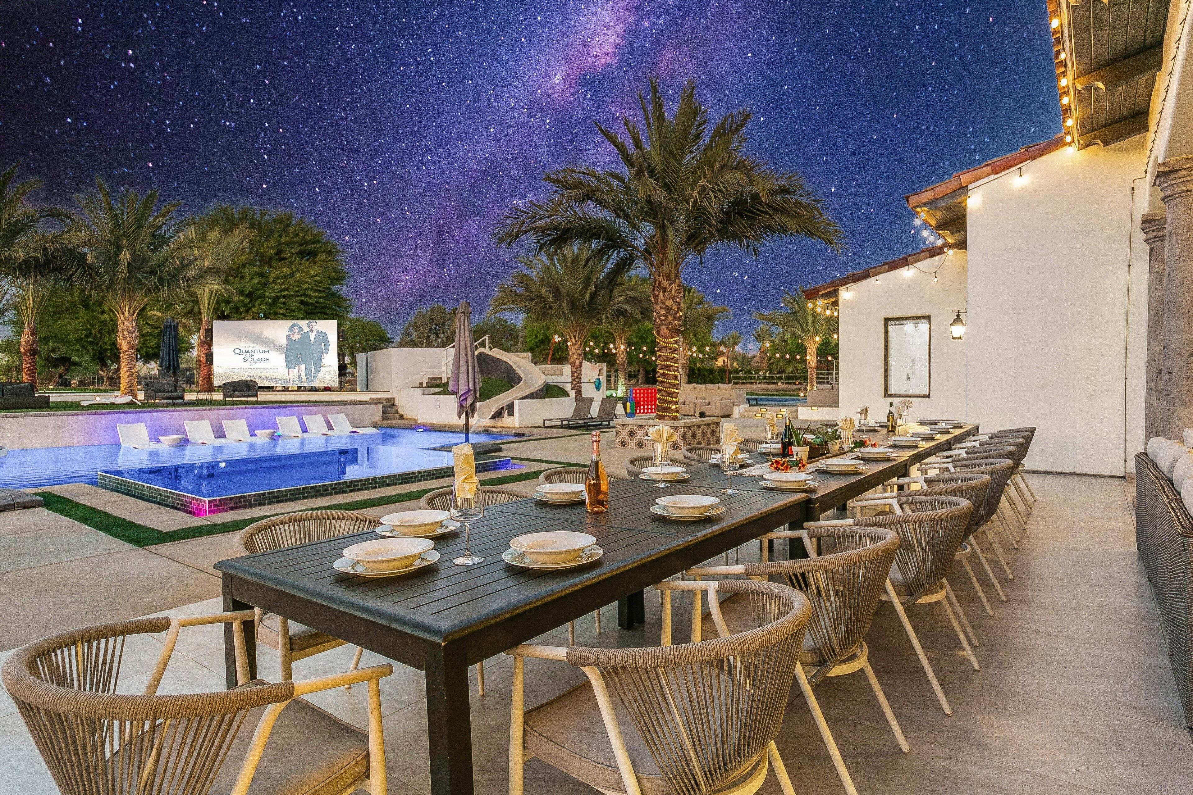 An outdoor dining area with a pool, starry sky, and palm trees.