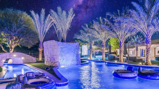 An outdoor swimming pool area with inflatable rafts, palm trees, and a stone structure. - The Stallion Estate Sleeps 24, Theater, Game Room, Pickle Ball (Indio)