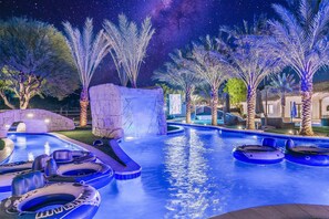 An outdoor swimming pool area with inflatable rafts, palm trees, and a stone structure. - The Stallion Estate Sleeps 24, Theater, Game Room, Pickle Ball (Indio)