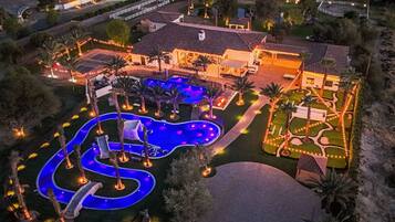 Una casa grande con piscina, rodeada de palmeras y senderos bien iluminados.