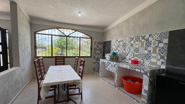 A kitchen with a dining table, chairs, a window with a view, tiled backsplash, and a refrigerator. - Casa rodeada de naturaleza  (Zacatlán)