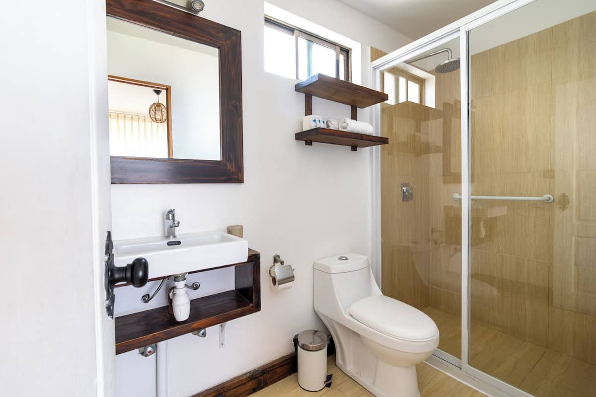 A bathroom with a toilet, sink, mirror, and shower.