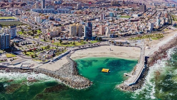 An aerial view of a coastal city with dense urban development, a large sandy beach, and a rocky shoreline. - Hostal Geosol (Antofagasta)