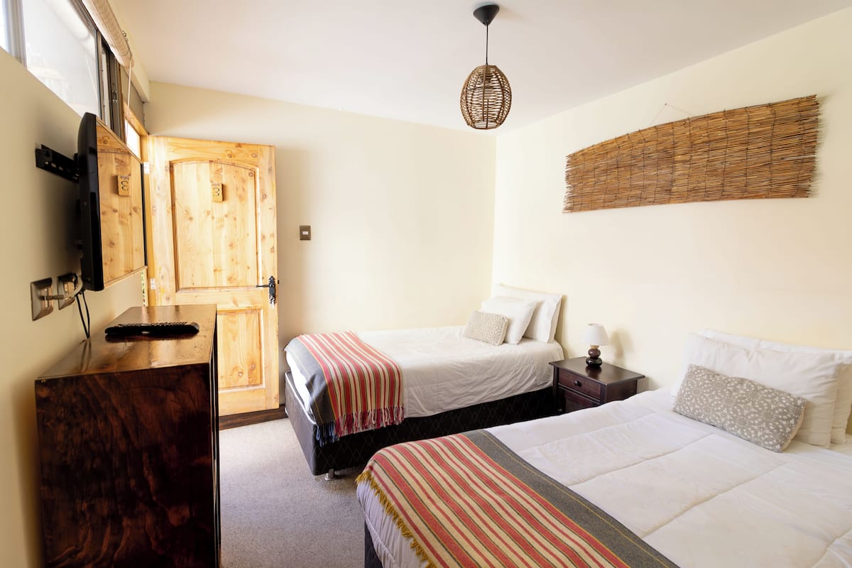A bedroom with two beds, a wooden wardrobe, a desk, and a wall-mounted artwork.