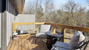A wooden deck with a fire pit and two chairs, a grill, and a propane tank.
