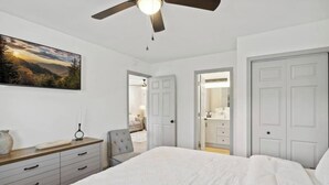 A bedroom with a large bed, a ceiling fan, a dresser, and a painting on the wall.