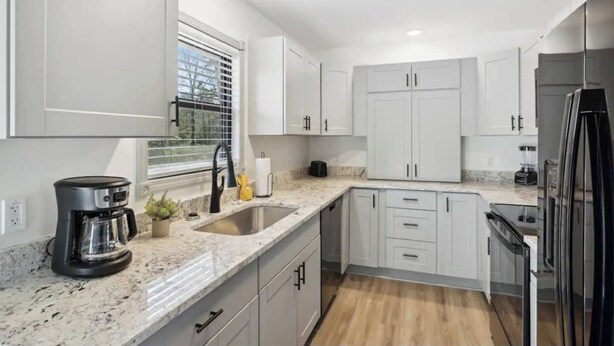 A modern kitchen with white cabinets, a granite countertop, a coffee maker, a sink, and a refrigerator.