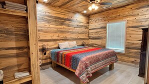 Una habitación con paneles de madera, una cama, un ventilador de techo y una ventana con persianas.