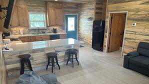 Una cocina moderna con armarios de madera, encimera de granito y refrigerador negro. Hay dos taburetes y un banco en la zona del comedor.