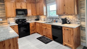 Cocina con gabinetes de madera, encimeras de granito, estufa negra, microondas y lavavajillas.