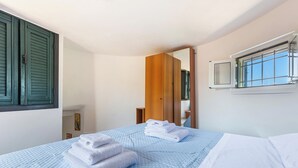 Habitación de hotel con cama, ventana con contraventanas, espejo y puerta que da a otra habitación.