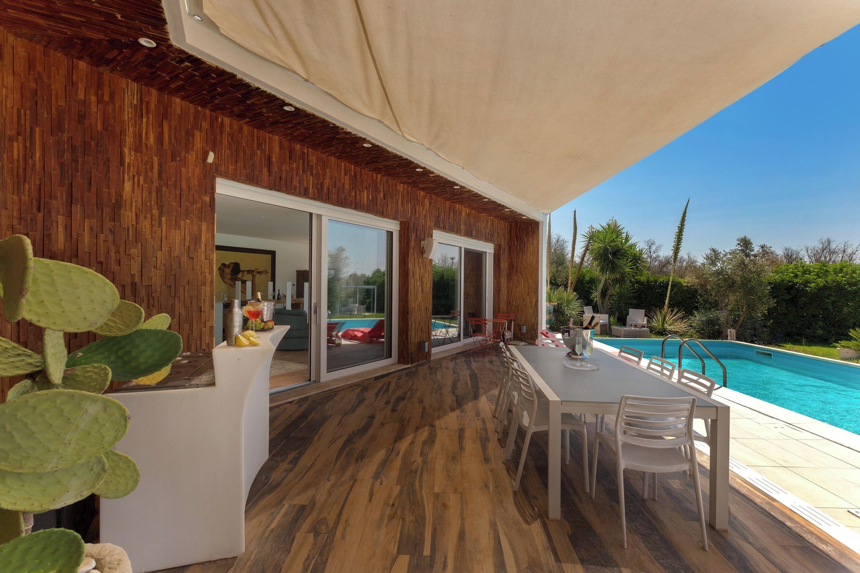 Ein moderner Essbereich im Freien mit Blick auf einen Pool, Holzboden und einer überdachten Terrasse.