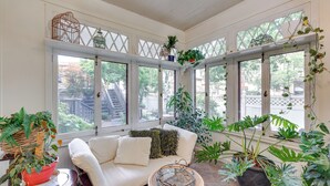 Une pièce baignée de lumière, avec un canapé blanc, un fauteuil en osier et diverses plantes en pot.