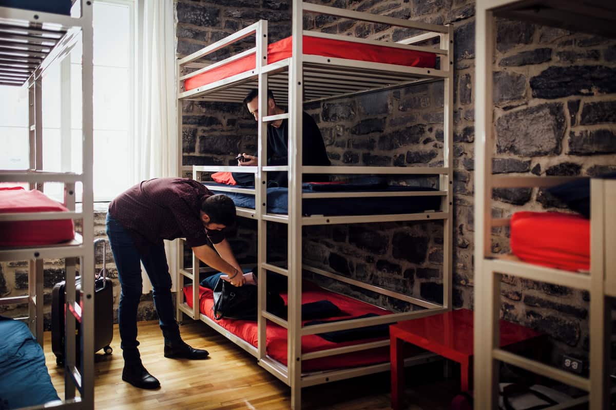 A bunk bed room with a stone wall, a suitcase, and a person adjusting a bag.