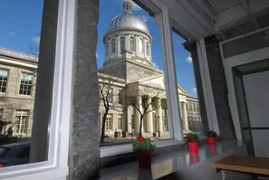 A view through a window of a building with a large dome, potted plants on the windowsill, and a bench inside. - Auberge Alt Hostel (Montréal)