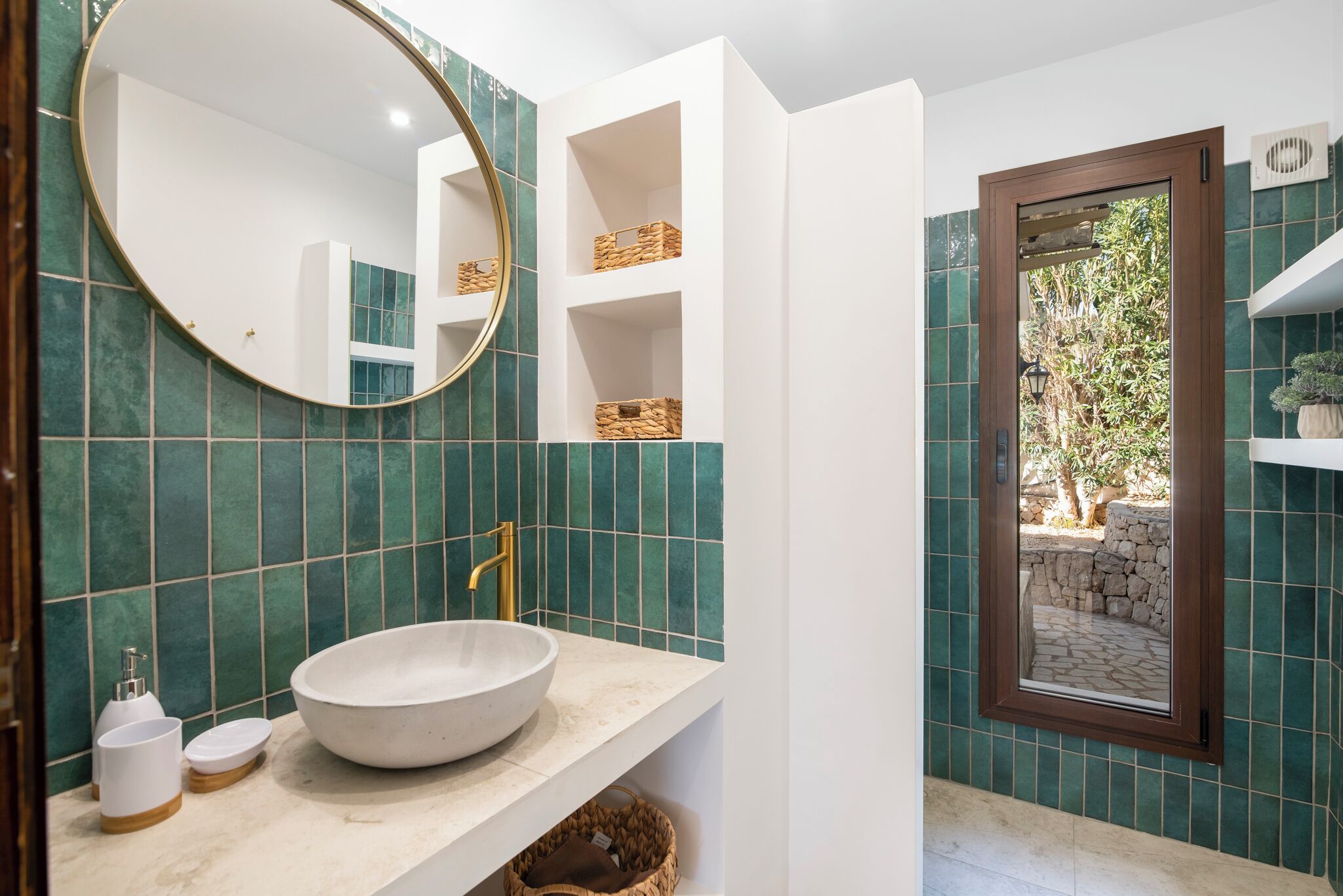 Un baño con un espejo redondo, un lavamanos blanco y paredes de azulejos verdes.