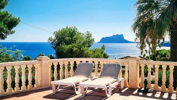 Un espace aménagé au bord de la piscine, avec deux chaises longues, une piscine carrelée et une vue sur la mer et une montagne en arrière-plan.