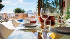 Une table à manger dressée avec des assiettes, des verres et un saladier rouge, donnant sur une piscine et des palmiers.