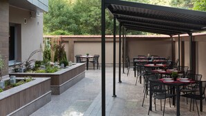 Un patio al aire libre con varias mesas y sillas, un área de estar cubierta y un jardín ajardinado.