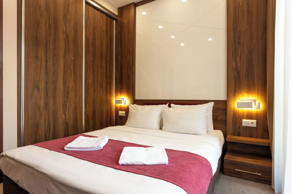 A hotel room with a large bed, wooden paneling, two bedside tables with lamps, and a carpeted floor.