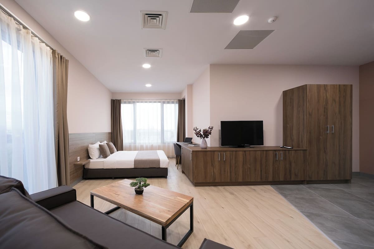 A modern hotel room with a bed, a sofa, a wooden coffee table, a TV, and a wardrobe.