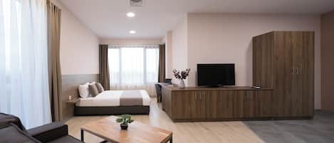 Ein modernes Hotelzimmer mit einem Bett, einer Couch, einem Holztisch, einem Fernseher und einem Kleiderschrank.