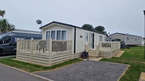 A mobile home with a fenced deck and a small porch. - Welcoming 3 Bedroom Caravan 2 Min Walk to Beach (Par)