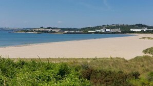 A beach with a sandy shore and a clear blue sky. There are buildings in the background, and greenery along the coastline. - Welcoming 3 Bedroom Caravan 2 Min Walk to Beach (Par)