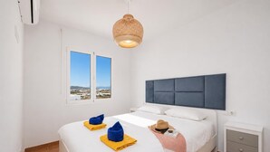 Un dormitorio con cama, una mesita de noche, una ventana con vistas y una lámpara colgante.