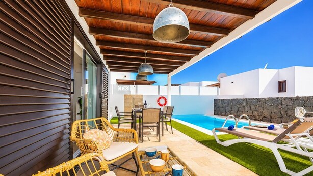 Un espacio al aire libre techado con piscina, muebles de mimbre y un muro de piedra.