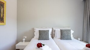 Ein Hotelzimmer mit zwei Betten, weißen Laken, grauen Kissen, einem Nachttisch mit Lampe und einem Gemälde an der Wand.