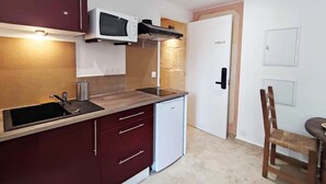 A compact kitchen with a microwave, sink, and a small refrigerator. There is a door labeled 'CAESAR' and a chair near a table. - Studio Caesar - Air conditionning (Arles)