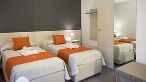 Une chambre d’hôtel avec deux lits, chacun recouvert d’une couverture et de plusieurs oreillers orange, une table de chevet avec une lampe et un grand miroir au mur.