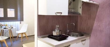 Una cucina compatta con un piano di lavoro bianco, un lavello e una pentola su un fornello portatile.