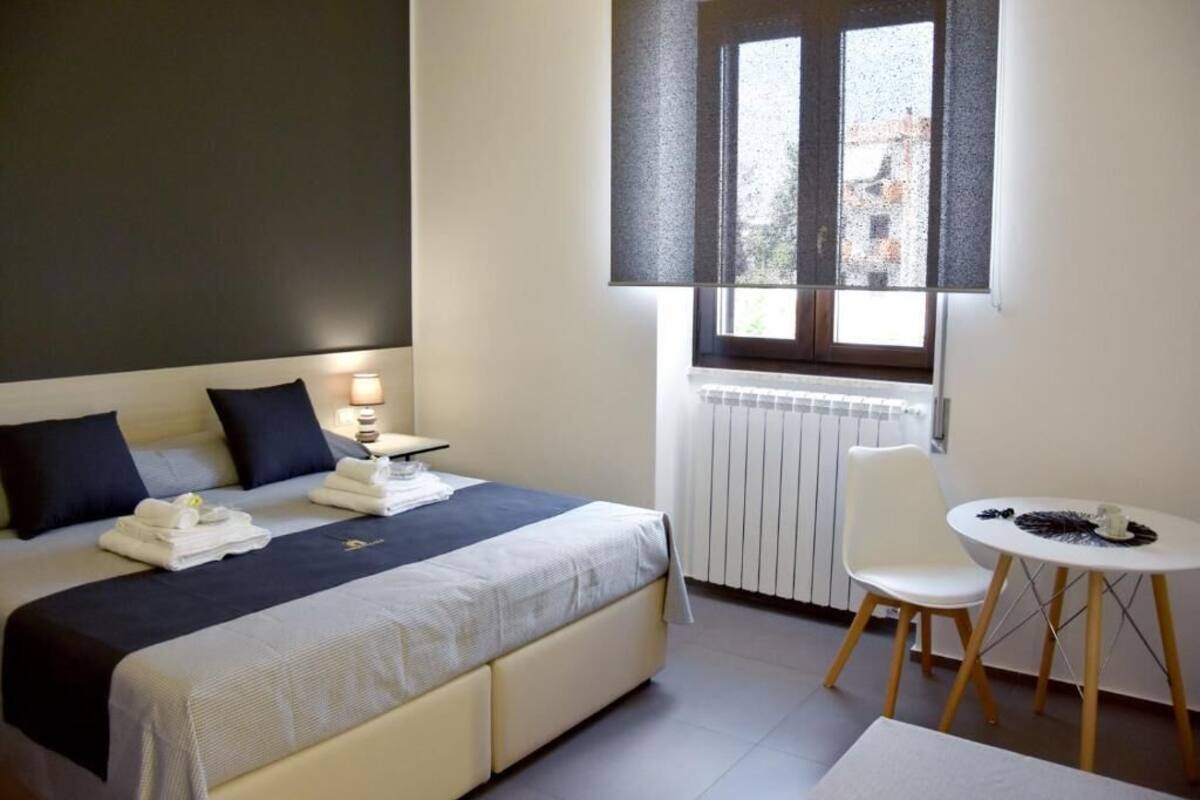 A bedroom with a bed, bedside table, chair, and a small table with a lamp.