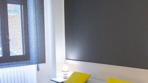 Une chambre d’hôtel moderne avec un grand lit, une table de chevet avec une lampe et une fenêtre équipée de stores.