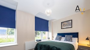 A modern bedroom with a large bed, a nightstand, a window with a view, and a ceiling light.